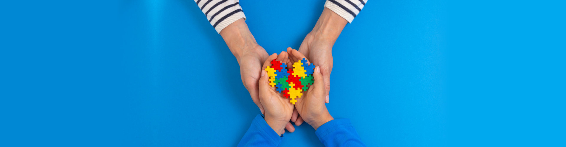 Woman and child hands holding puzzle heart on light blue background