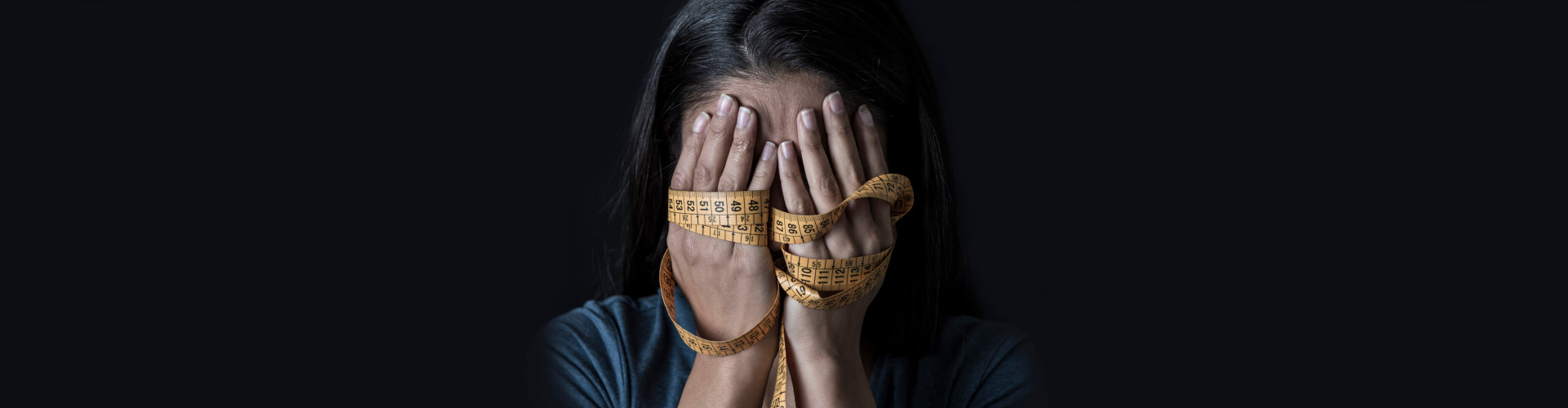 A woman covering her face while holding a tape measure